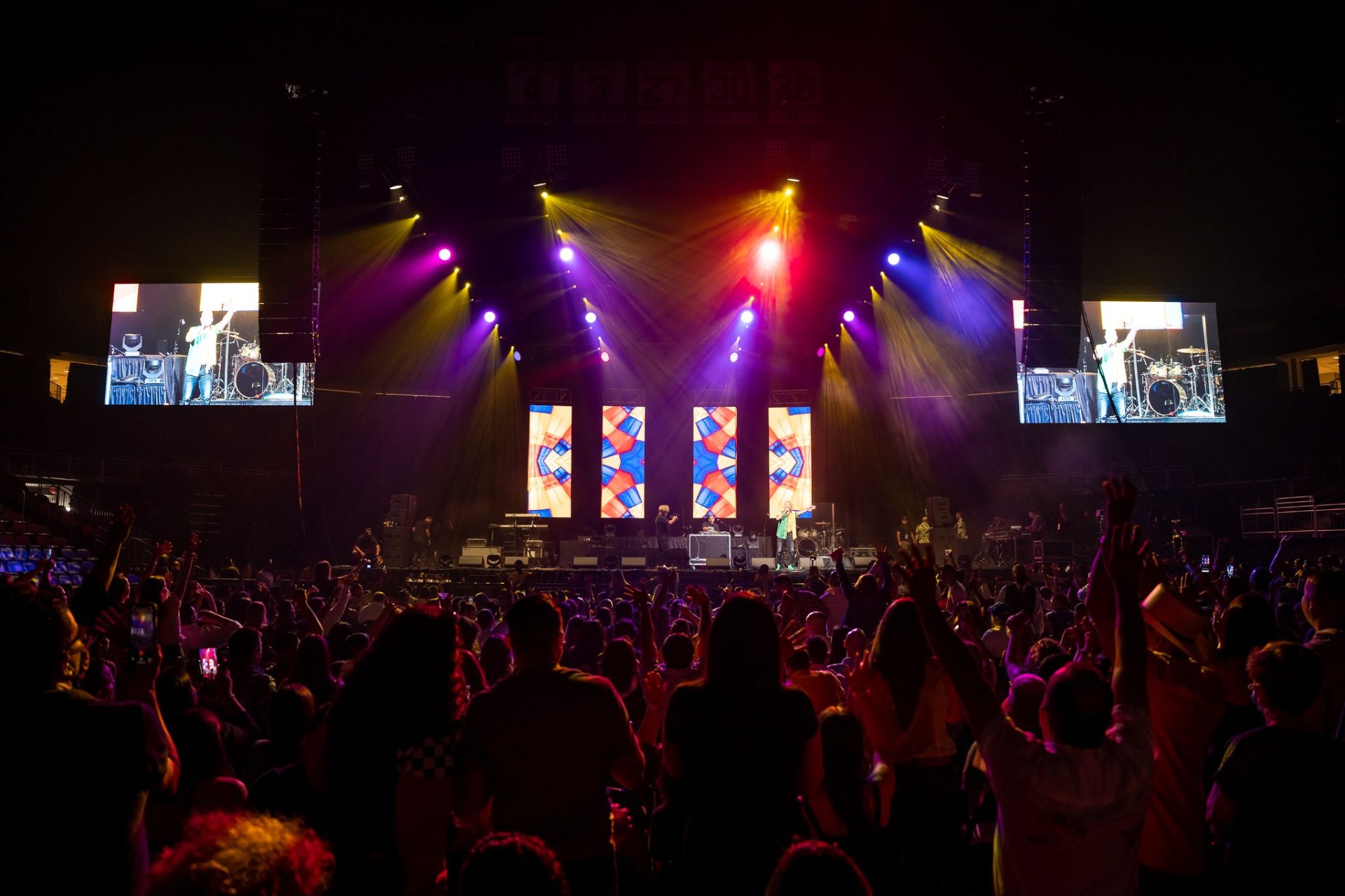 Vista del público en arena con luces moradas y rojas